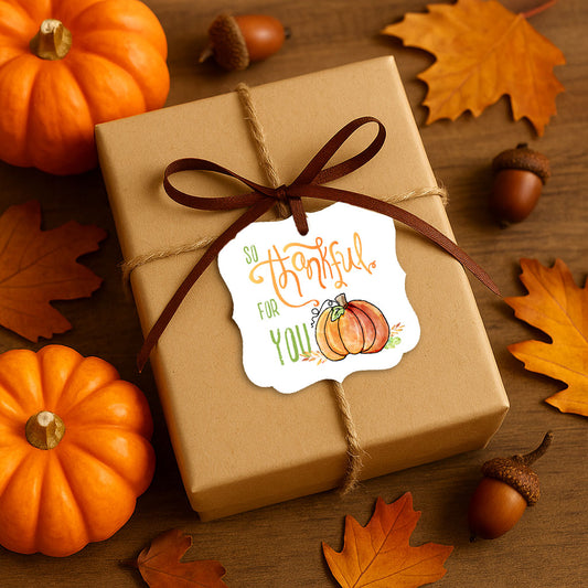 Thanksgiving gift wrapped in kraft paper and tied with twine and a brown ribbon, featuring a “So Thankful For You” pumpkin tag surrounded by mini pumpkins and autumn leaves.