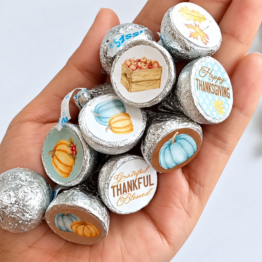 Hand holding silver-wrapped chocolates with blue pumpkin Thanksgiving stickers, showing the size of the round candy labels.