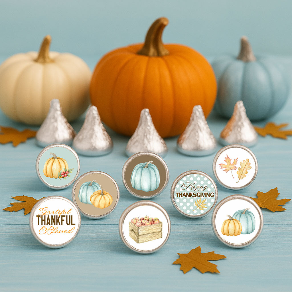 Blue pumpkin Thanksgiving stickers on silver-wrapped chocolates arranged with orange and cream pumpkins on a blue background.