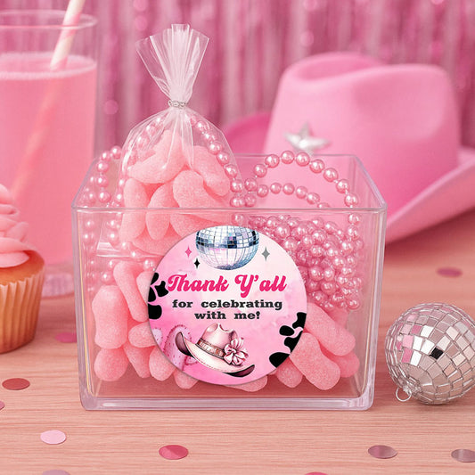 Disco Cowgirl thank you sticker on clear favor box filled with pink candy, styled with beads, disco ball, and cowgirl hat.