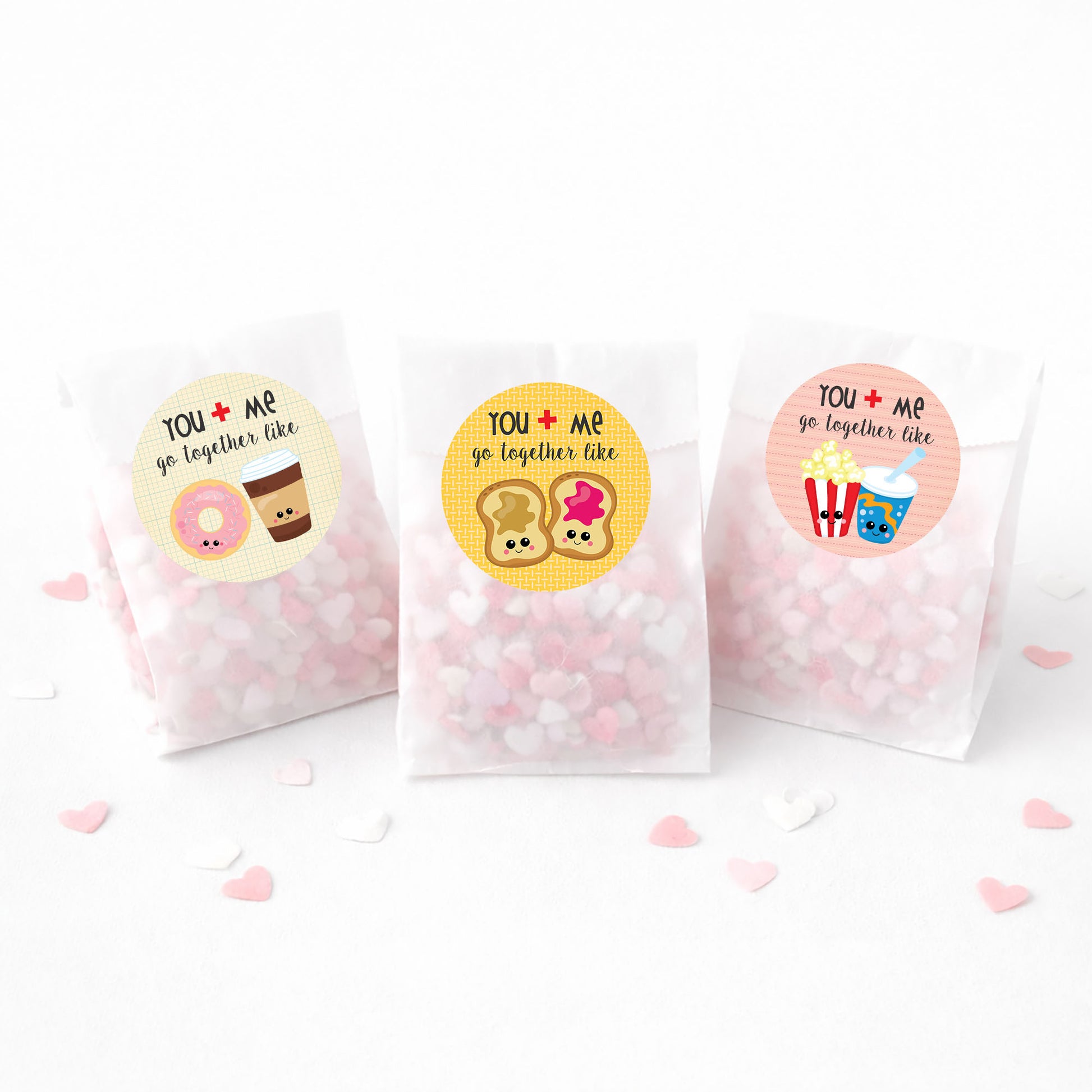 Three small bags with colorful stickers and pink heart-shaped candies on a white background