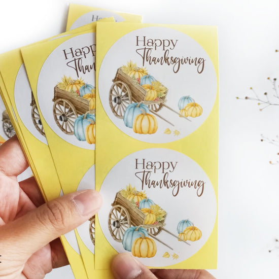 Set of Thanksgiving stickers held in hand, showing multiple 2.5 inch round labels with watercolor pumpkin design.