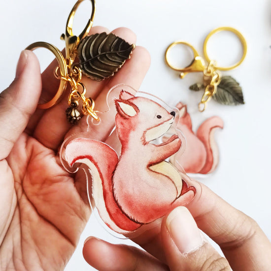 Cute squirrel acrylic keychain held in hand with gold clasp and leaf charm showing woodland animal accessory design