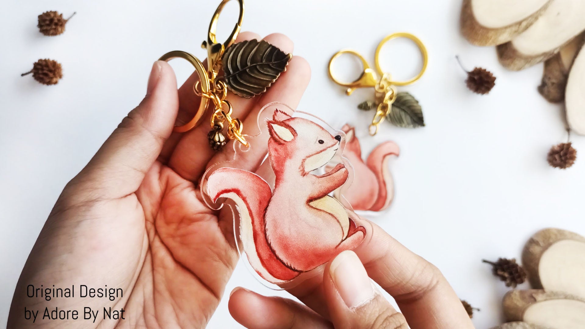 Cute squirrel acrylic keychain held in hand with gold clasp and leaf charm showing woodland animal accessory design