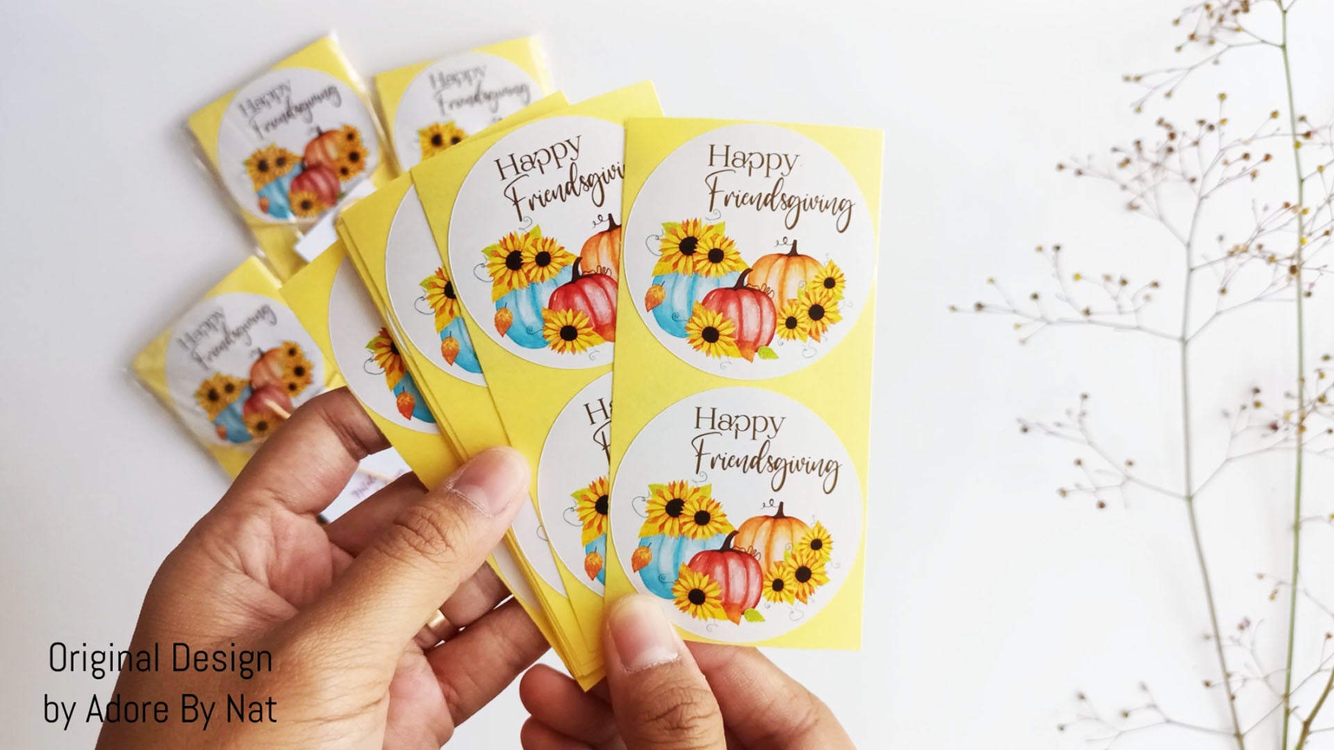 Hand holding set of Happy Friendsgiving stickers with rustic-modern pumpkin and sunflower design for fall favors