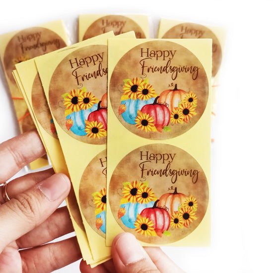 Hand holding Friendsgiving pumpkin sunflower stickers, rustic fall labels for bags, jars, envelopes, and favors