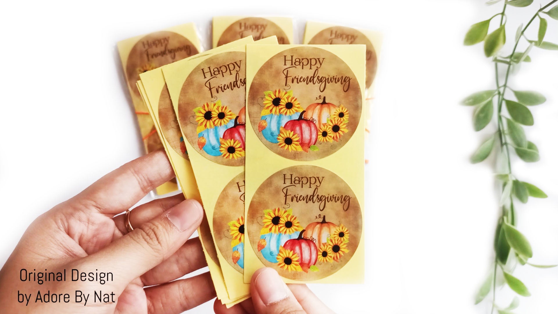 Hand holding Friendsgiving pumpkin sunflower stickers, rustic fall labels for bags, jars, envelopes, and favors